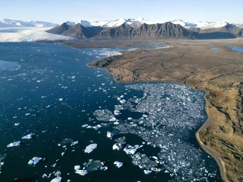 Aerial view of Jökulsárlón glacier lagoon, icebergs drifting in dark water below the glacier and the mountains of the South Coast