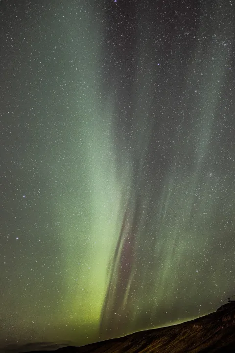 Green and violet northern lights filling a starry sky above a dark ridge in Iceland