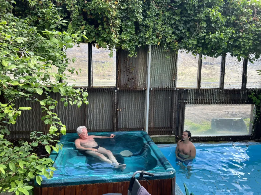 Guest relaxing in a hot tub under leafy branches while his guide stands in the pool alongside