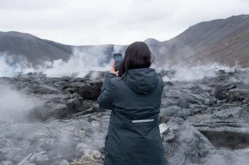 Silhouette of a traveller watching a river of glowing lava and red-lit steam during a night eruption on the Reykjanes Peninsula
