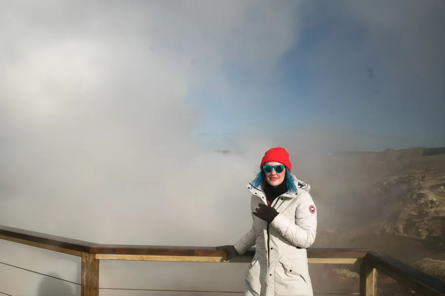 Traveller in a red hat at the Gunnuhver boardwalk on Reykjanes, geothermal steam drifting across the frame