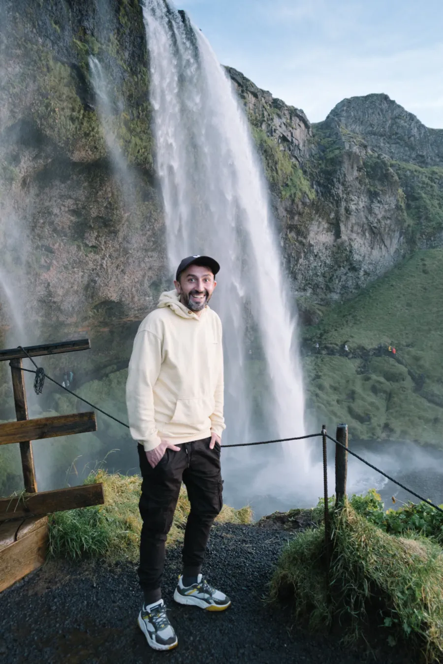Traveller smiling on the path in front of Seljalandsfoss, the waterfall falling behind him