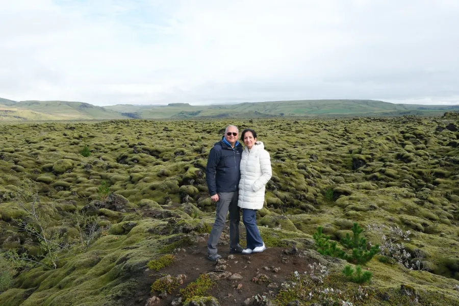 Couple standing together on a vast moss-covered lava field under a pale sky
