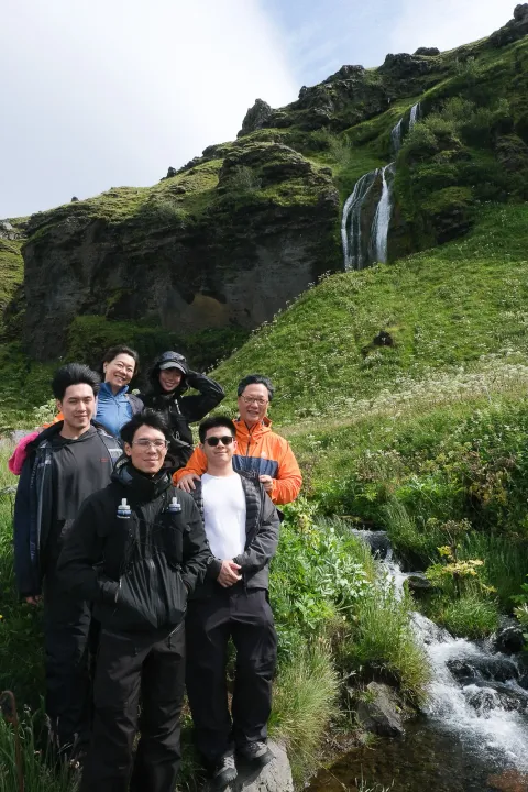 Group of travellers by a small waterfall and green hillside on the South Coast in summer