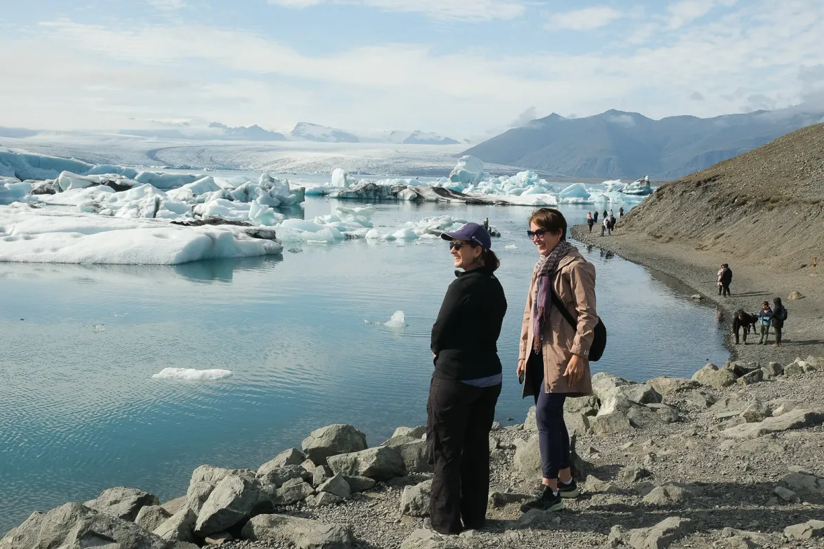 Two travellers on the rocky shore of Jökulsárlón glacier lagoon, icebergs and the glacier behind them