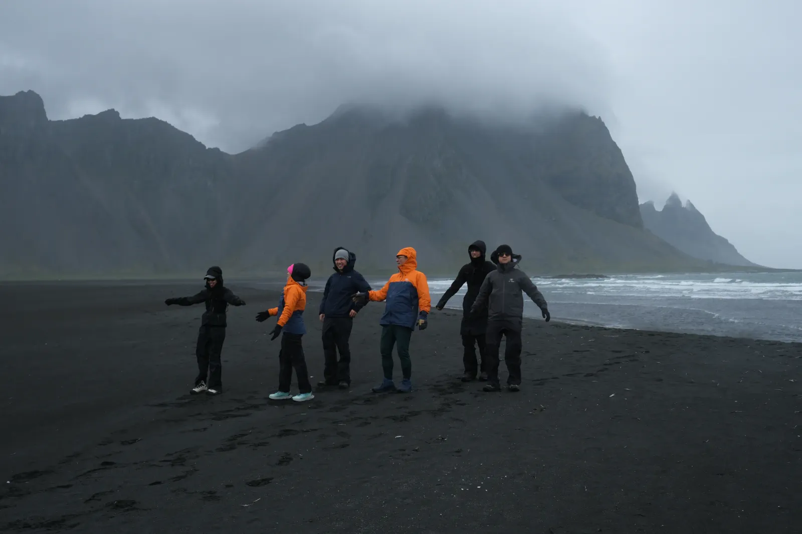 Group of six travellers on the black sand at Stokksnes, the Vestrahorn mountain under low cloud behind them