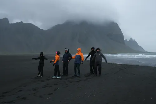 Group of six travellers on the black sand at Stokksnes, the Vestrahorn mountain under low cloud behind them