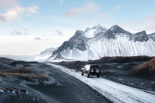Black 4x4 on a snow-dusted track crossing black sand towards the snow-covered Vestrahorn mountain in Iceland