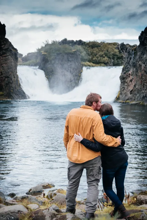 Couple embracing as they look at the twin Hjálparfoss waterfalls